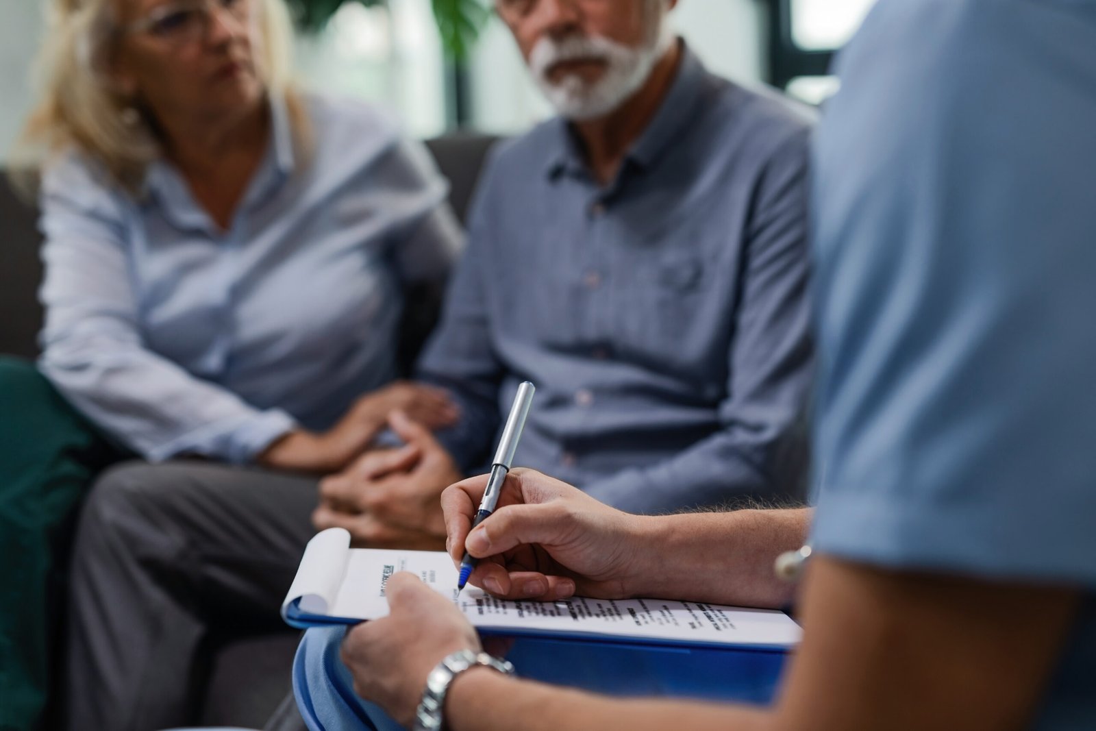 Unrecognizable male doctor writing medical report while visiting senior couple at their home.